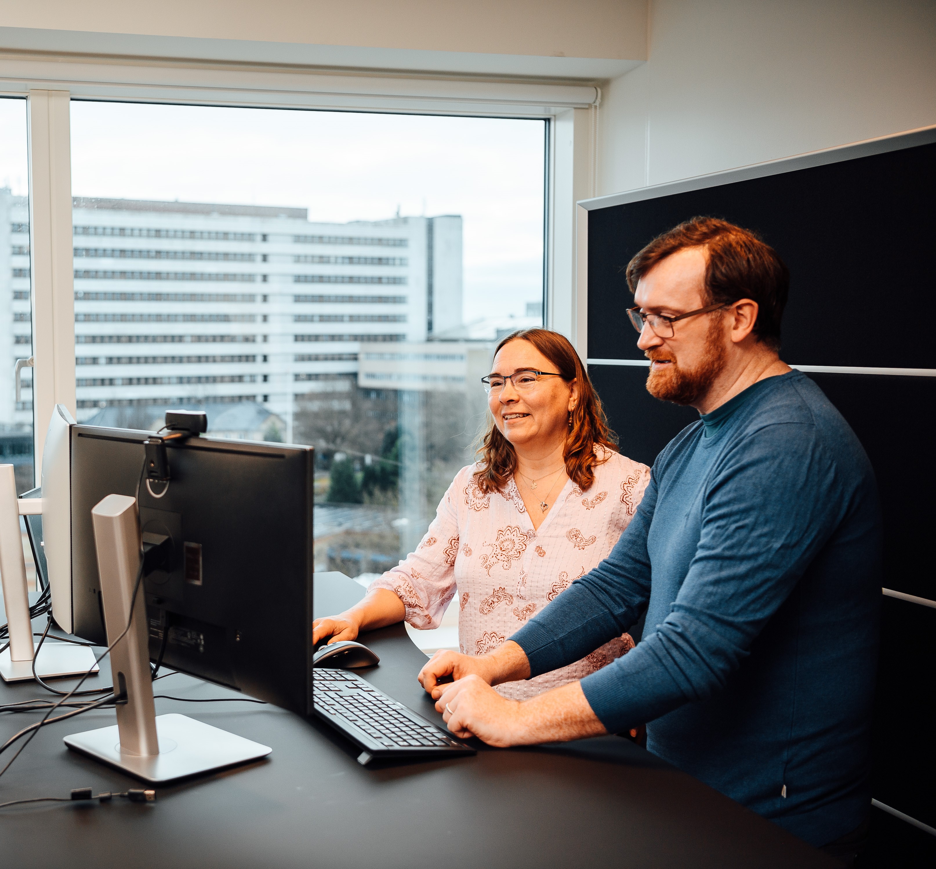 Man wearing glasses working at a desktop computer in a bright office environment