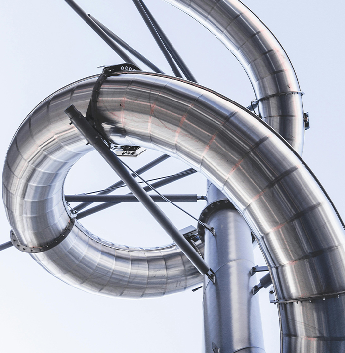 Close-up of large, intertwined, shiny metal pipes against a light sky, showcasing complex industrial engineering